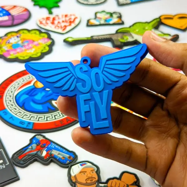 Vibrant blue custom PVC patch with 3D raised wings, held in hand to show durable rubber texture.