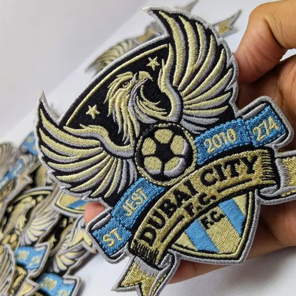 Luxury custom embroidered crest featuring an eagle design with high-detail gold metallic thread on black fabric.