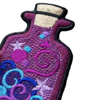 Close-up of a custom embroidered potion bottle patch highlighting a thick, protective merrowed overlock border for a classic look.