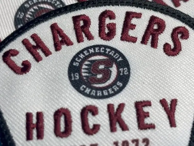 Close-up of a custom hybrid sports patch featuring a high-detail printed center logo and maroon embroidered text for a hockey team.
