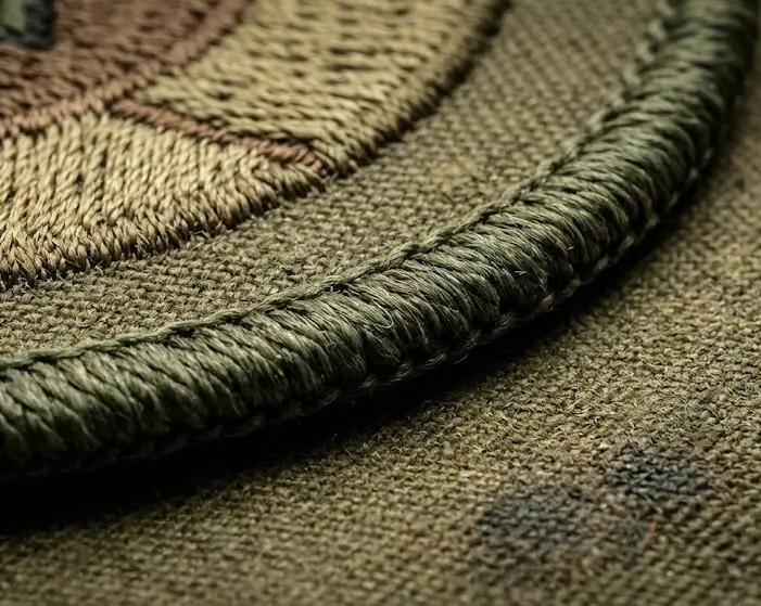 Macro detail of a thick merrowed overlock border on a custom olive green embroidered patch, showing the durable wrap-around stitching.