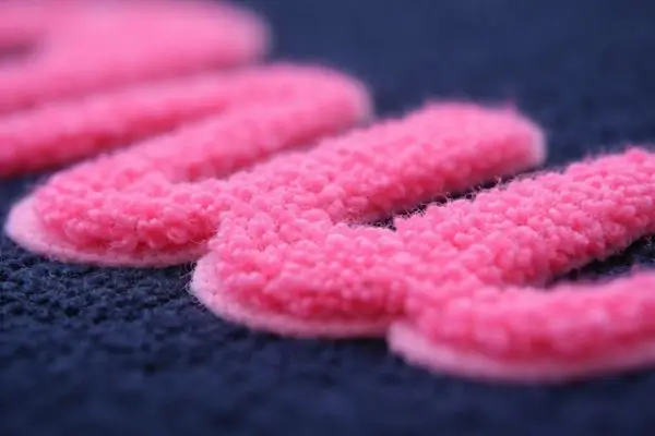 Extreme close-up of a pink chenille patch showing its soft, fuzzy towel-like texture on navy blue fabric.