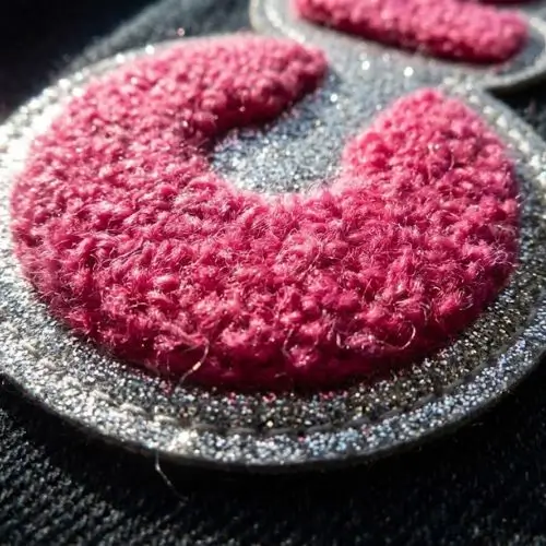 Silver metallic glitter felt border on a pink chenille letterman patch.