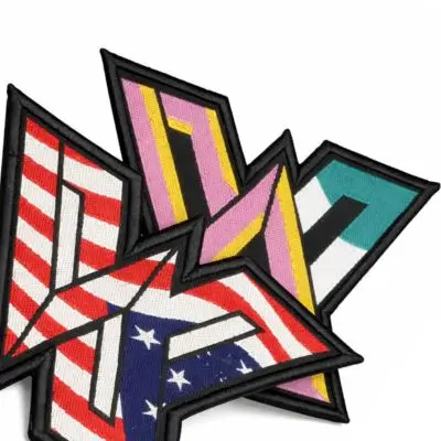Two custom jagged-shaped woven patches featuring a high-definition American flag and colorful geometric patterns with thick black borders.