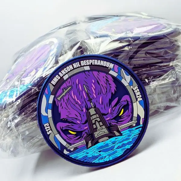 A detailed circular submarine morale PVC patch displayed in front of a bulk production run of bagged patches for a marine client.