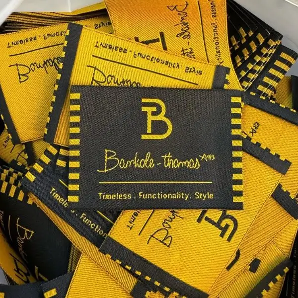 A pile of custom black and gold woven clothing tags for the brand Bankole-Thomas.