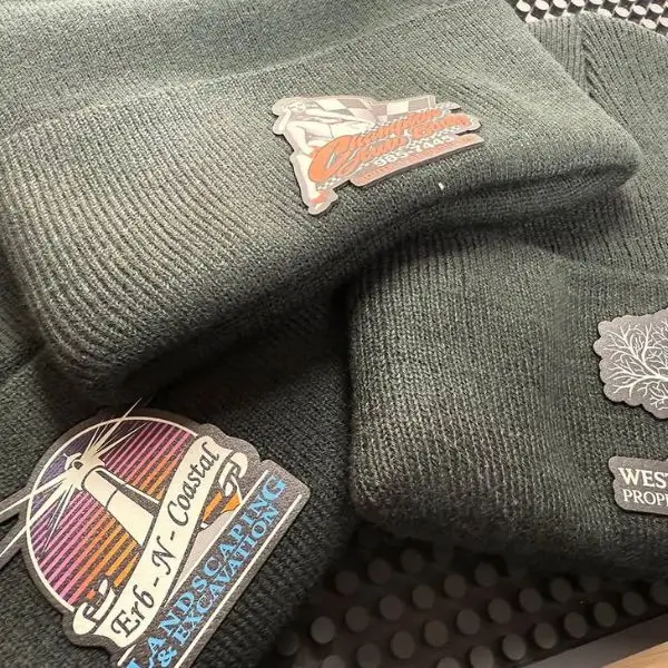 Custom printed patches heat-pressed onto olive green beanies, showing detailed branding application for workwear.